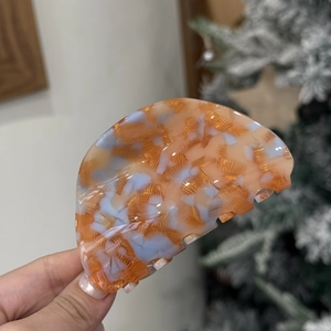 Close-up of a semi-circular acetate hair claw clip with colorful marble texture and glossy finish