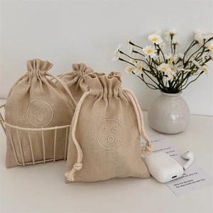 Macro view of linen drawstring bags with embroidered smile face and floral decor