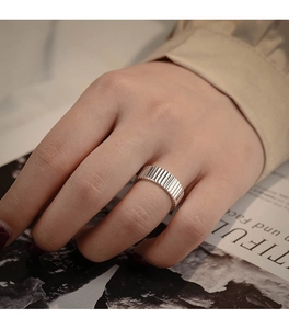Close-up of minimalist silver ring with vertical textures worn on a hand against magazines