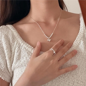 Close-up of minimalist heart pendant necklace and textured silver ring on model