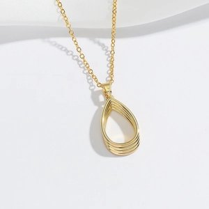 Minimalist gold teardrop hollow pendant necklace on white background with silk texture