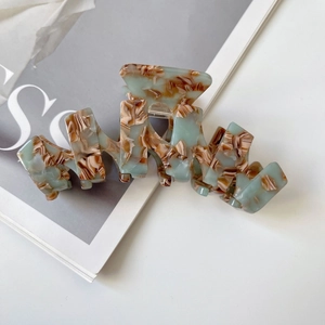 Detail view of large wave-shaped acetate hair claw clip with marble texture on magazine