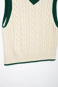 Macro view of cable knit texture and green striped ribbed V-neckline on white vest