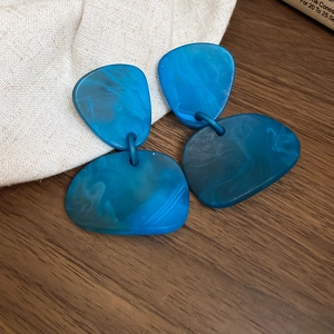 Close-up of blue geometric resin earrings with marble texture on wooden and linen surface