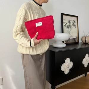 Close-up of red corduroy makeup bag with white label held by hand in home setting