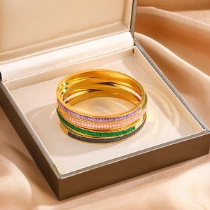 Detail of four gold-plated stainless steel bangles with colorful zircon inlays on satin