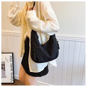 Dettaglio di una borsa a tracolla in nylon nero indossata da una modella su sfondo neutro