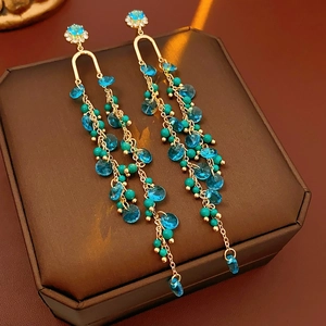 Detail of gold tassel earrings with blue faceted beads and green stone on jewelry box