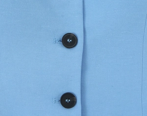 Close-up of black four-hole buttons on light blue plain fabric of the two-piece set