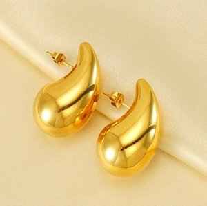 Detailed view of polished 18K gold hollow teardrop earrings on champagne silk fabric