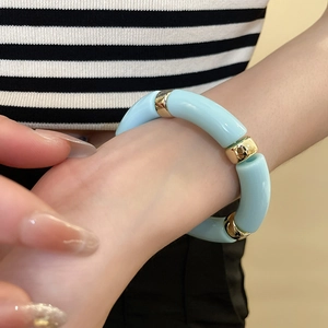 Detail of light blue acrylic geometric bracelet with gold metallic spacers on wrist