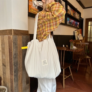 Detailed view of large white pleated tote bag with brand label in a cafe setting