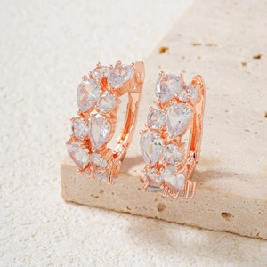 Close-up of rose gold drop earrings with white zircon clusters on a stone texture surface