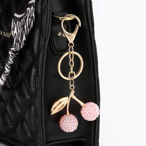Porte-clés cerise en cristal rose sur sac matelassé noir avec fermoir doré élégant