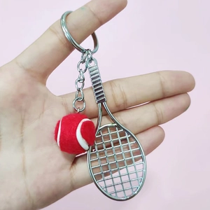 Detail showing a mini red felt tennis ball and silver racket keychain held in hand