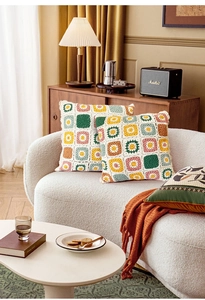 Detail of colorful hand-crocheted granny square pillow cover on a modern white sofa