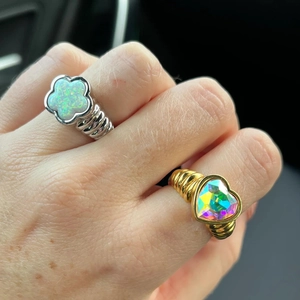 Detail of gold heart rainbow stone and silver flower opal rings on finger