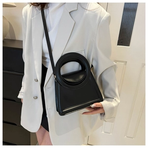 Elegant black crossbody bag with a circular hollow handle shown with a white blazer