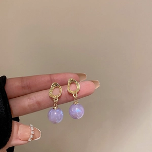Close-up of golden irregular textured earrings with purple pearlescent beads in hand