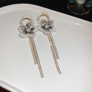 Détail de boucles d'oreilles fleur en tulle avec perle et longs pompons en strass
