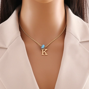 Close-up of gold letter K pendant and blue evil eye bead on a rope chain necklace