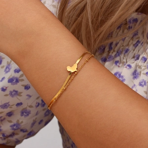 Detail of layered gold bracelet featuring snake chain and heart-shaped map pendant