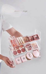Three-tier clear acrylic organizer showing storage for makeup palettes and lipsticks