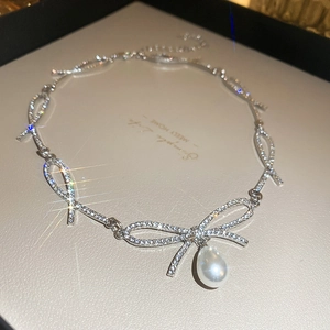 Close-up of silver bow necklace with pavé crystals and a teardrop pearl pendant
