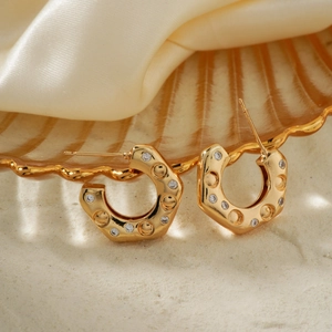 Elegant gold U-shape earrings with zircon inlay on a stylish textured glass plate