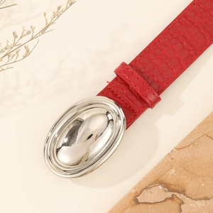 Red crocodile embossed leather belt with a large oval silver buckle on a beige background