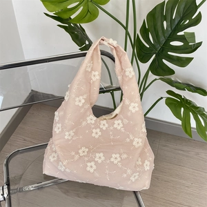 Detail of floral embroidery on light pink tote bag placed on a transparent chair