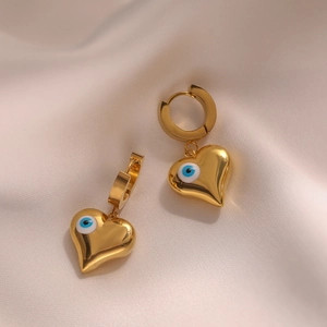 Gold stainless steel heart earrings featuring a blue evil eye on white silk fabric