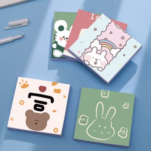 Flat lay of four cute cartoon mini notebooks with bear and rabbit designs on a blue desk
