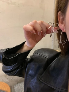 Close-up of silver bow hoop earrings showing woven wire detail on model's ear