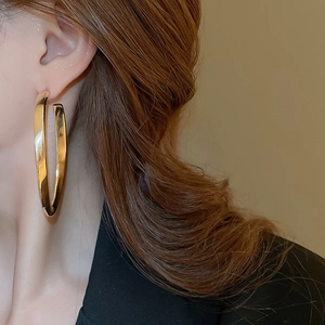Close-up of model wearing large oversized gold-tone hoop earrings with a sleek metallic finish