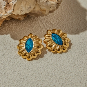 Detailed shot of gold scallop-edged earrings with marquise-cut blue crystals on natural stone