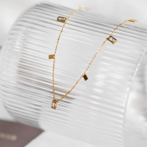 Elegant gold chain necklace with rectangular crystal pendants on a textured glass bottle