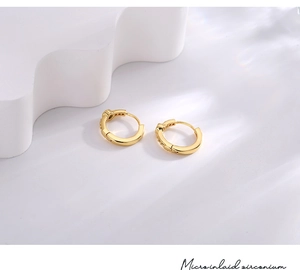 Close-up of golden hoop earring featuring micro-inlaid blue zircon on minimalist base