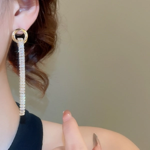 Detail of long geometric gold earrings with cubic zirconia fringe on a model's ear
