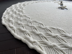 Close-up of cream white knitted Christmas tree skirt with cable patterns on wood floor