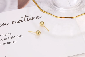 Macro detail of polished gold ball stud earrings on a minimalist decorative display