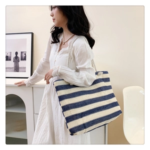 Detailed view of a striped woven straw tote bag with rope handles worn by a model