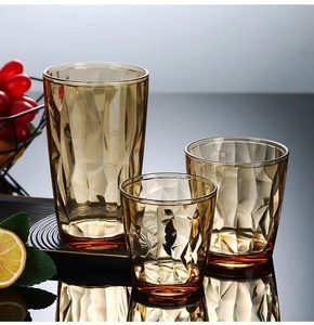 Three amber acrylic cups with geometric facets and decorative fruit on a dark table
