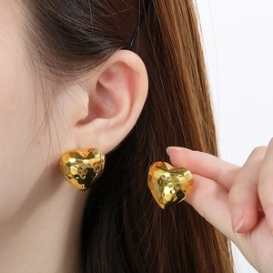 Detail of gold hollow heart studs featuring a unique hammered metal texture on ear