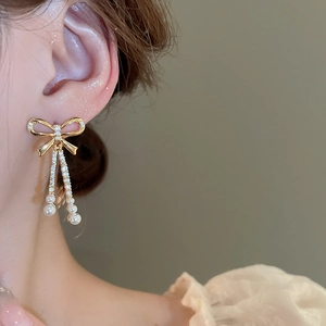 Close-up of gold-plated bow earrings with pavé rhinestones and hanging pearl tassels
