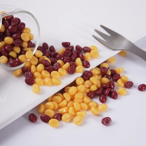 Miniature wax seal beads in yellow and dark red pouring from a glass onto a white plate