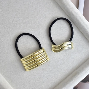 Detail of minimalist gold alloy hair ties with striped and wavy metal decorative accents