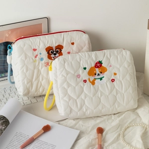 Detail of cute dog embroidery on white heart-quilted cosmetic bag with red zipper