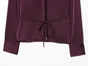 Détail d'une blouse en satin violet foncé avec taille à cordon et embouts dorés