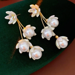 Macro detail of gold flower tassel earrings with white pearls on green velvet
